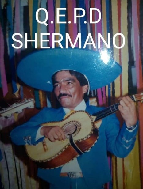The letters q, e, p & d can be seen and underneath the word "shermano", meaning brother. The picture is of a man dressed in mariachi attire holding a guitar.
