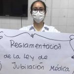 A photo of Idalia Medina wearing a mask and holding a sign that reads "Regulación de la ley de Jubilación Médica", which translates to Regulation for the medical retirement laws.